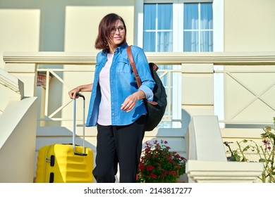 Middle Aged Woman With Backpack With Suitcase On The Steps Of House Porch