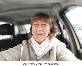 Middle aged woman in a car taking a selfie while enjoying a drive. Female mature driver posing inside car. Funny happy tourist girl in alone travel - Powered by Shutterstock