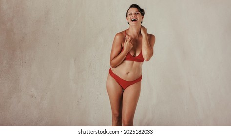 Middle aged woman celebrating her natural body. Body positive and happy woman smiling cheerfully while wearing red underwear against a studio background. Woman standing alone in a studio.