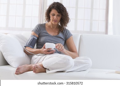 Middle Aged Woman Checking Blood Pressure With Sphygmometer On Sofa