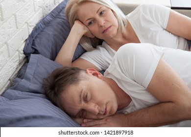 Middle Aged Woman Covering Ears While Man Snoring In Bed At Home