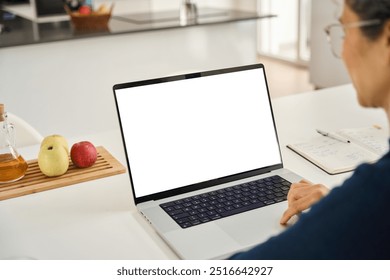 Middle aged woman customer looking at white mock up blank screen using laptop computer at home table doing online shopping, searching on web. Website mockup display template. Over shoulder view. - Powered by Shutterstock