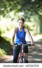 Middle Aged Woman Cycling Along Country Lane