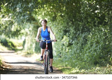 Middle Aged Woman Cycling On Country Road