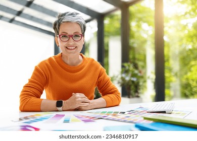 Middle aged woman designer working in her office, employee confident in expertise and style of creativity. Cheerful lady 50s interior design professional using computer and color palette, copy space - Powered by Shutterstock