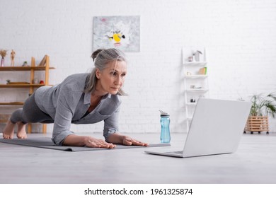 Middle Aged Woman Doing Plank On Fitness Mat Near Laptop