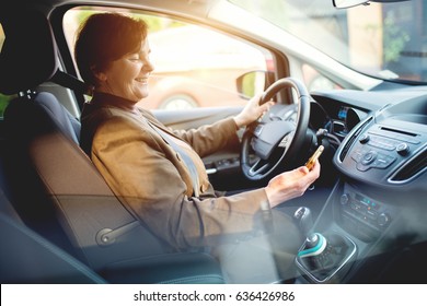 Middle aged woman driving a car looking at mobile phone. - Powered by Shutterstock