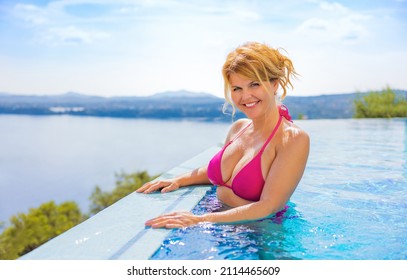 Middle aged woman enjoying vacation, standing in infinity pool with beautiful Mediterranean sea view