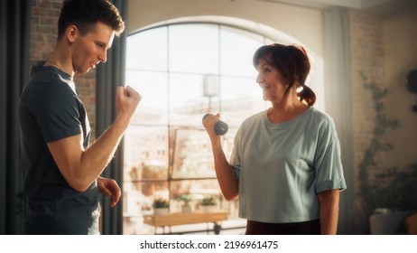 Middle Aged Woman Exercising At Home With Personal Trainer. Elderly Female Strengthening Arm Muscles With Dumbbell Workout. Young Athlete Supporting And Guiding Her Through The Training.