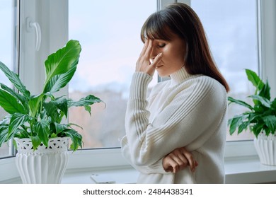 Middle aged woman experiencing stress depression mental pain, at home near window - Powered by Shutterstock