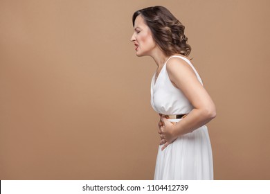 Middle Aged Woman Feeling Stomach Pain, Unwell. Have Stomach Pain . Emotion And Feeling Concept. Studio Shot, Indoor, Isolated On Light Brown Background