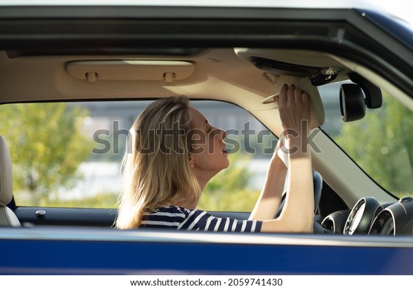 Middle aged woman fixing makeup looking in rear
view mirror driving car. Female driver distracting from road and
heavy traffic jam. Happy smiling positive lady drive vehicle on
trip to summer vacation