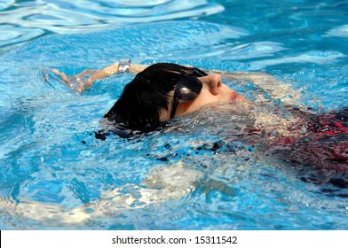 Middle Aged Woman Gets Her Exercise In The Swimming Pool.  She Is Wearing Sunshades And A Black And Red Swimsuit.