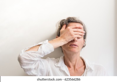 Middle Aged Woman With Grey Hair With Hand Covering Face Against White Wall (selective Focus)