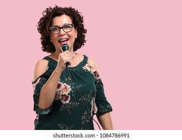 Middle aged woman happy and motivated, singing a song with a microphone, presenting an event or having a party, enjoy the moment