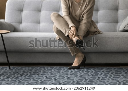 Middle aged woman in high heeled shoes sitting couch, taking stiletto footwear off, touching painful ankle, feeling pain in joint, leg muscle, suffering from problems with veins, Cropped shot of feet