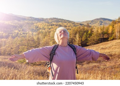 Middle Aged Woman Hiking And Going Camping In Nature. Happy Senior With Outstretched Arms With Backpack Walking In The Forest