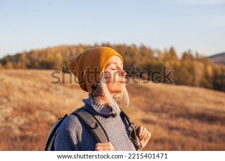 Middle aged woman hiking and going camping in nature. Person with backpack walking in autumn forest
