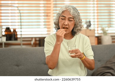 Middle aged woman holding glass of fresh water and taking medicines. Elderly healthcare, medication concept - Powered by Shutterstock