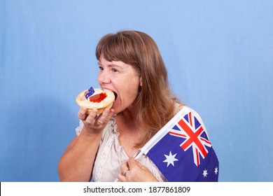 A Middle Aged Woman With Light Brown Hair Eating A Traditional Meat Pie While Holding A Flag At An Australia Day Celebration.