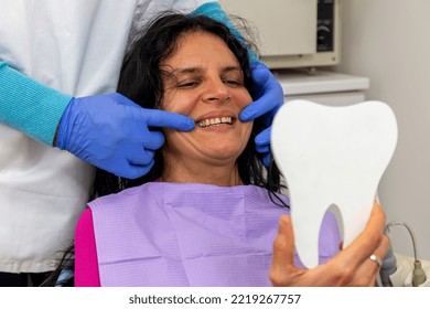 Middle Aged Woman  Looking At Her Teeth In The Mirror At Dentist's Office.Concept Of Happy Patient And Dentist