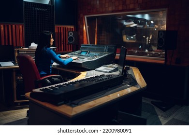 Middle aged woman music producer working on a mixing soundboard while in her sound studio. Recording studio control desk. Professional music studio. Working on control desk to produce new song. - Powered by Shutterstock