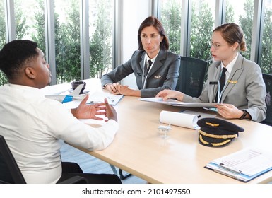 Middle aged woman pilot and team interview African American man for his career job opportunity. Aviation businesspeople collaborating in creative meeting discussing idea around table in modern office. - Powered by Shutterstock