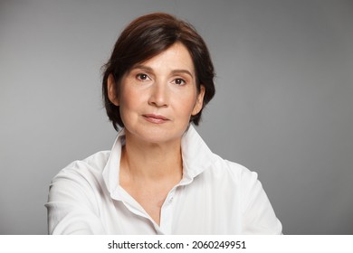 Middle Aged Woman Portrait Wearing White Shirt Against Gray Solid Background.