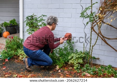 Middle aged woman putting a foam cover on an outdoor spigot as part of fall outdoor chores getting ready for winter

