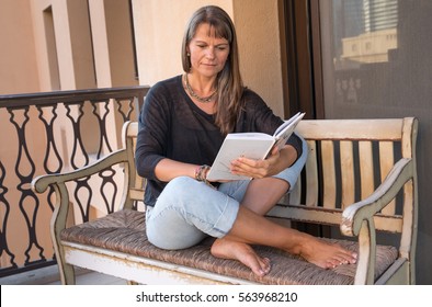 Middle Aged Woman Reading A Book On A Balcony.