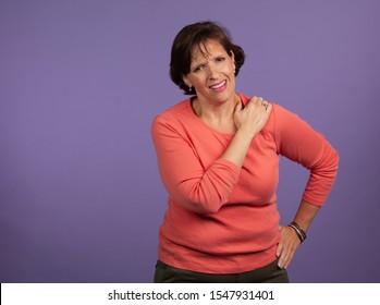 Middle Aged Woman With Shoulder Pain Holding Her Left Shoulder And Making A Pained Expression. Chronic Pain Concept Image.