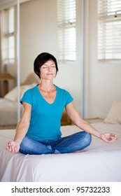 Middle Aged Woman Sitting On Bed Doing Yoga Meditation