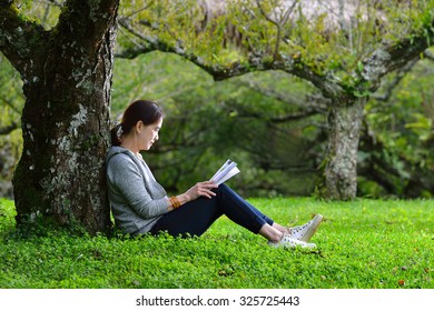 Middle Aged Woman Sitting Under A Tree Reading A Book