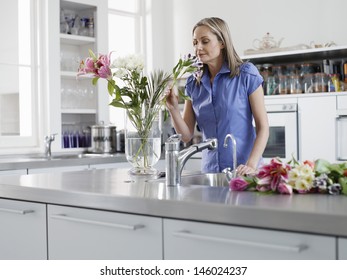 Middle Aged Woman Smelling Flowers In Vase In Kitchen