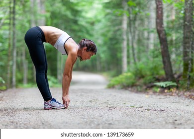 Middle Aged Woman Stretching In The Woods On A Dirt Road Before A Run