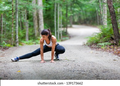 Middle Aged Woman Stretching In The Woods On A Dirt Road Before A Run