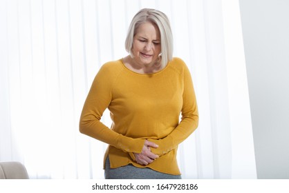 Middle aged woman suffering from abdominal pain while at home. Concept photo with indicating location of the pain. Health care concept