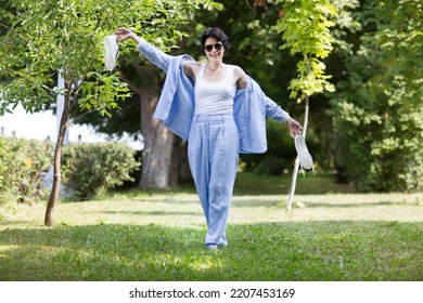 Middle Aged Woman  In A Suit Without Sneakers Walks Barefoot On The Grass In The Park. Enjoying The Little Things. Lykke Concept. Relaxation Concepts
