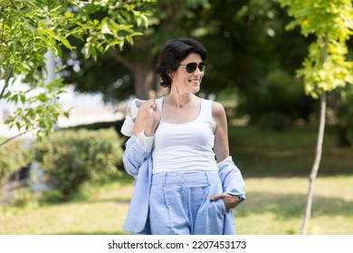 Middle Aged Woman  In A Suit Without Sneakers Walks Barefoot On The Grass In The Park. Enjoying The Little Things. Lykke Concept. Relaxation Concepts
