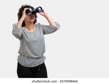 Middle aged woman surprised and amazed, looking with binoculars in the distance something interesting, concept of future opportunity