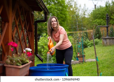 Middle aged woman taking water for watering flowers in her garden, because it is very dry season.