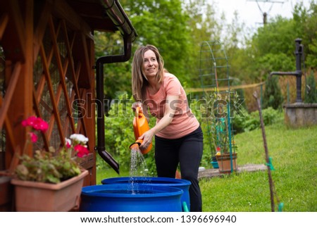 Middle aged woman taking water for watering flowers in her garden, because it is very dry season.