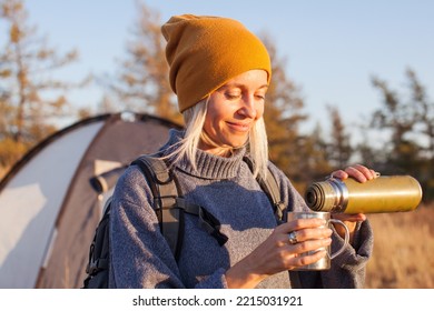 Middle Aged Woman Travel And Camping Alone At Fall Forest. Happy Female Relaxing After Hiking, Drinking Tea