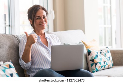 Middle aged woman using laptop in the sofa pointing with hand and finger up with happy face smiling - Shutterstock ID 1127632478