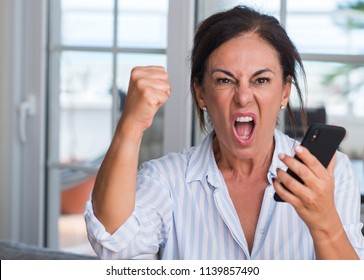 Middle Aged Woman Using Smartphone Annoyed And Frustrated Shouting With Anger, Crazy And Yelling With Raised Hand, Anger Concept