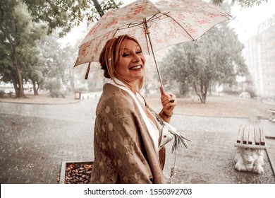 Middle Aged Woman Walking In Rain With Umbrella At The Street Park. 