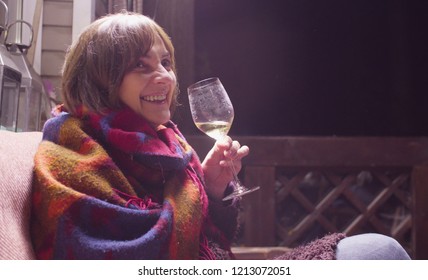 Middle Aged Woman In Warm Clothes Sitting On The Sofa On The Terrace Of A Country House And Drinking Wine