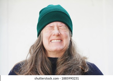 Middle aged woman wearing a navy blue sweater and a green beanie cap has long thick brown and gray hair and stands outside against a white background                               - Powered by Shutterstock