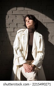 Middle Aged Woman  In A White Cloak Relaxing Against A Gray Wall. Copy Space. 