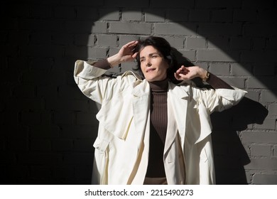 Middle Aged Woman  In A White Cloak Relaxing Against A Gray Wall. Copy Space. 